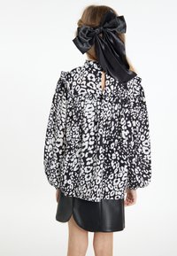 Blå og hvid leopardprint bluse med puffærmer, flæsedetaljer og nøglehul tilbage. Kombineret med en sort lædernederdel.