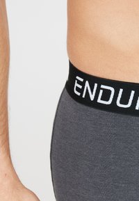Grijze katoenen boxershorts hebben een zwarte elastische tailleband met witte tekst "ENDURE". De textuur is glad en de pasvorm sluit nauw aan op het lichaam.