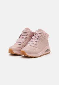 Zapatillas de deporte rosa claro con acentos texturizados, parte superior transpirable y un collar acolchado. Cuenta con una suela de goma y amortiguación de aire integrada.