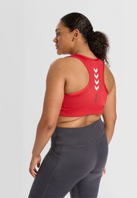 Röd sportbh med racerback-design, som har vita chevron-detaljer på ryggen. Mörkgrå högmidjade leggings med sidofickor.