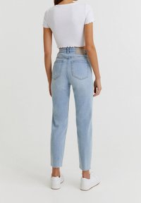 Jeans de tiro alto en azul claro, con pierna recta y dobladillo deshilachado, combinados con un top corto de canalé blanco, usados con zapatillas blancas.