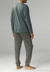 Męski zestaw odzieży domowej składający się z zielonej bluzy z długim rękawem i szarych spodni dresowych. Miękka tkanina o luźnym kroju oraz ściągaczach na kostkach.