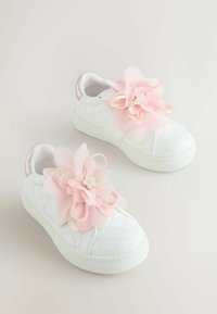 Valkoiset tennarit, joissa on teksturoitu kukkakuvaus, koristeltuna suurilla vaaleanpunaisilla kangaskukilla ja pienellä helmisomisteella sivussa.