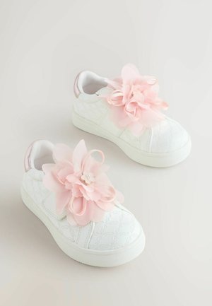 Valkoiset tennarit, joissa on teksturoitu kukkakuvaus, koristeltuna suurilla vaaleanpunaisilla kangaskukilla ja pienellä helmisomisteella sivussa.