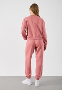 Hanorac din bumbac roz și pantaloni jogger asortați, cu manșete elastice. Setul are o croială confortabilă și un design simplu, asociat cu adidași albi.