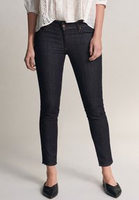 Mörkblå skinny jeans i denim med medelhög midja, subtila sömdetaljer och beskuren fåll. Bärs med spetsiga svarta ballerina.