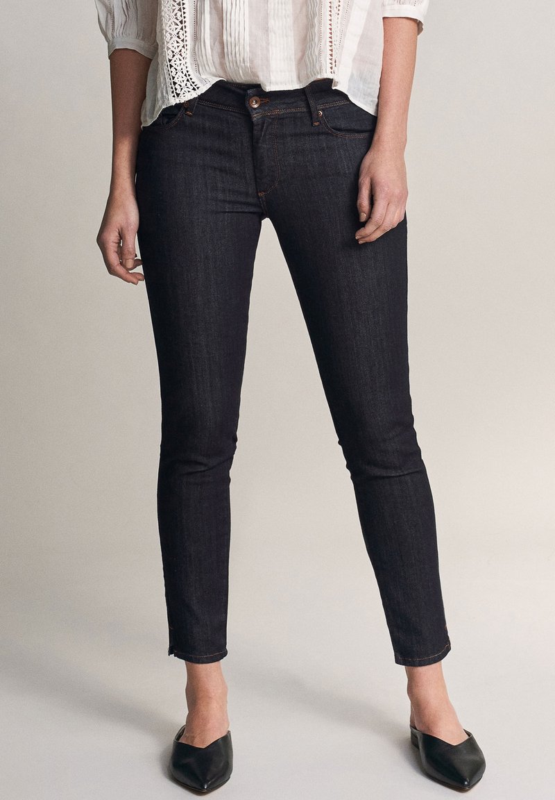 Mörkblå skinny jeans i denim med medelhög midja, subtila sömdetaljer och beskuren fåll. Bärs med spetsiga svarta ballerina.