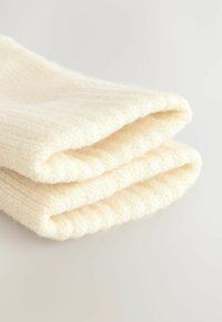 Calze in maglia di colore crema, morbide e piegate, realizzate con un tessuto testurizzato, caratterizzate da un design a coste e un aspetto accogliente.