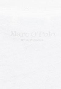 Hvidt stof med en glat tekstur, der har et let præg af logoet "Marc O'Polo" med teksten "EST. I STOCKHOLM" nederst.