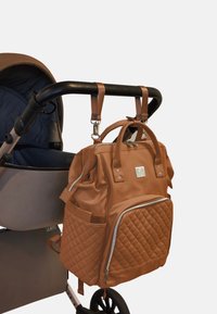 Bolsa de pañales mochila acolchada marrón con asas dobles y correas desmontables, sujeta a un carro de bebé. Material suave, acentos de hardware plateados.