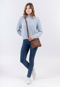 Borsa a tracolla in cuoio marrone con tasca con zip, accompagnata da un maglione a coste azzurro chiaro e jeans skinny blu scuro.