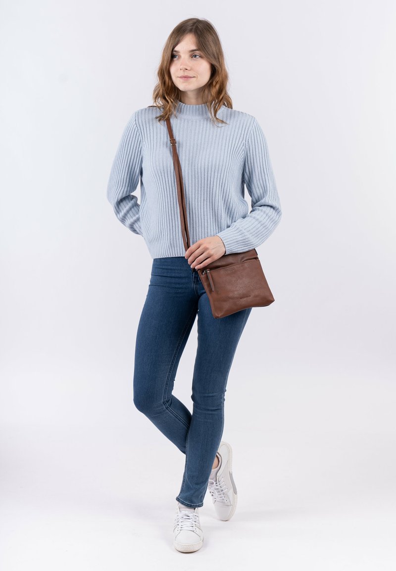 Borsa a tracolla in cuoio marrone con tasca con zip, accompagnata da un maglione a coste azzurro chiaro e jeans skinny blu scuro.