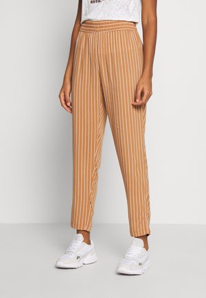 Tan stribede bukser med løs pasform, elastisk talje, tilspidsede ben og en glat stofstruktur, parret med hvide sneakers.