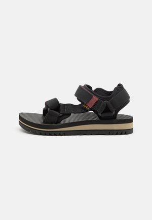Black sandals with adjustable straps, a textured footbed, and a two-tone sole featuring a dark top and light beige layer.