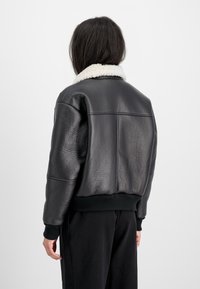 Veste bomber en cuir noir avec une surface texturée, col en shearling blanc, poignets et ourlet côtelés, vue de dos.