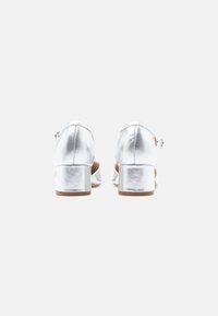 Ασημί μεταλλικά ψηλοτάκουνα παπούτσια με στρογγυλή μύτη, λουράκι στον αστράγαλο και τετράγωνη φτέρνα. Μοναδική υφή με μια υποτονική γυαλάδα.