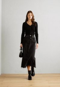 Crna majica s dugim rukavima sa zatvaračem u boji, u kombinaciji s crnom traper midi suknjom. Outfit je upotpunjen crnim čizmama do gležnja i malom torbicom.