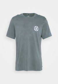 Camiseta de algodón gris con mangas cortas, cuello redondo y un pequeño logo en el pecho. Textura suave, ajuste estándar, sin estampados visibles.