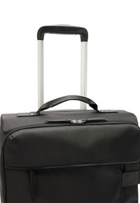 Czarna walizka z tkaniny z teleskopowym uchwytem, górnym uchwytem do noszenia i zamykaną kieszenią. Teksturowana powierzchnia z srebrnymi zamkami błyskawicznymi i akcentami.