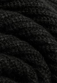 Nahaufnahme von weichem, dickem schwarzen Strickstoff mit sichtbarer Textur und flauschigen Fasern, die gefaltete Lagen zeigen.