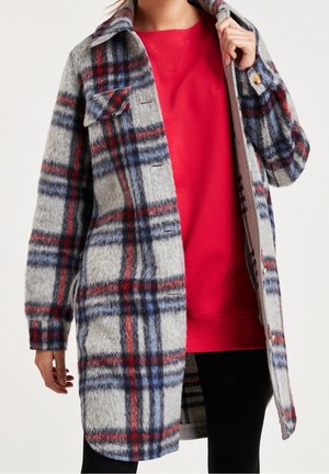 Cappotto a quadri in toni di grigio, rosso e blu; texture morbida e pelosa; chiusura a bottoni; due tasche frontali; indossato aperto sopra un felpa rossa.