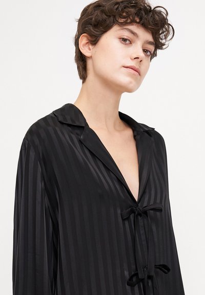 Camisa de satén negra con rayas verticales, con un collar muescado, un escote en V profundo y detalles atados en la parte frontal. Manga larga.