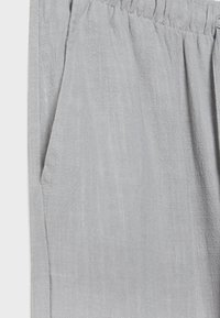 Harmaa kevyt kangas, jossa on teksturoitu pinta. Sisältää joustavan vyötärön ja sivutaskun, jossa on ommeltu yksityiskohta.