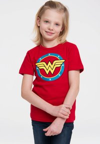Red cotton t-shirt featuring a yellow "W" logo with wings, encircled by a blue and red ring, accented with white stars.