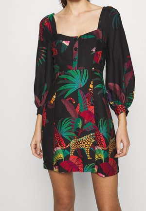 Femme portant une robe noire avec un imprimé feuilles tropicales colorées et léopard, un col carré et de longues manches bouffantes.