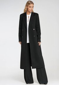 Długi czarny płaszcz z podwójnym zapięciem, wył участymi kołnierzem i teksturowanym materiałem. Posiada kieszenie po bokach i prosty krój dla dopasowanego wyglądu.