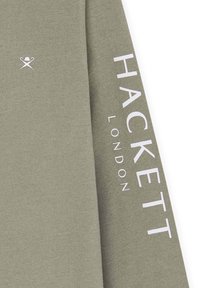 Helle olivgrüne Langarmbluse mit einem kleinen Logo und fett gedrucktem weißen Text "HACKETT LONDON" entlang des Armes. Weicher Stoff.
