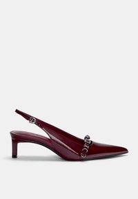 Escarpin à bride arrière en cuir verni bordeaux avec un bout pointu, un petit talon et des détails en métal sur la bride avant.