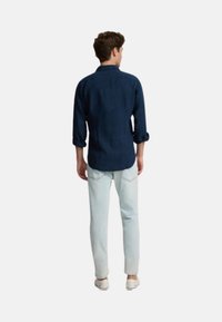 Camisa azul marino con mangas enrolladas, combinada con jeans celestes. Presenta un collar clásico y diseño de botones, con una textura suave.