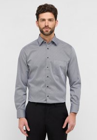 Camicia button-up in un motivo geometrico blu chiaro e bianco, maniche lunghe, colletto a punta e bottoni scuri. Tessuto morbido.