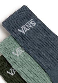 Ribbade strumpor i mörkgrön, dämpad grön och skifferblå. Varje strumpa har en vit "VANS"-logotyp över kanten. Mjuk stickad yta.