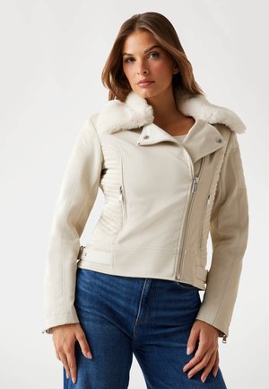 Giacca in pelle beige chiaro con colletto in pelliccia sintetica, chiusura frontale asimmetrica con zip, tasche laterali e dettagli a costine sui lati.