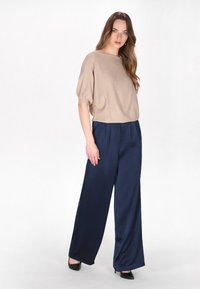 Beige struktureret top med korte pufærmer, parret med marineblå vide bukser. Sorte hæle fuldender outfittet. Enkelt og elegant design.