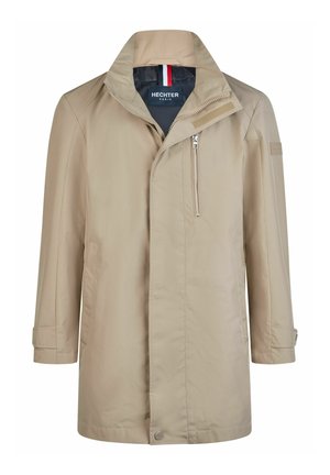 Trench-coat beige pour homme, longueur mi-mollet, avec col montant, poche poitrine zippée, sangles à velcro aux poignets et étiquette intérieure de marque.