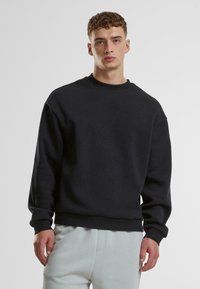 Schwarzer Rundhalsausschnitt-Sweatshirt aus dickem Baumwollstoff, mit gerippten Bündchen und Saum, getragen mit hellgrauen Sweatpants. Einfaches, minimalistisches Design.