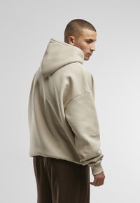 Sweat à capuche beige avec une coupe surdimensionnée, en tissu épais, avec des épaules tombantes et des poignets côtelés, associé à un pantalon marron foncé.