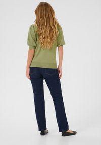 Top verde a maglia con maniche corte e puff; abbinato a jeans diritto blu scuro e scarpe nere basse; vista da dietro, capelli lunghi visibili.