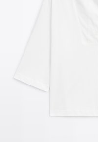 Weißes Kurzarmhemd mit V-Ausschnitt, das ein schlichtes Design und eine glatte Textur aufweist. Leicht übergroßer Schnitt mit einfachem Saum.