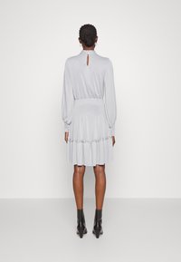 Robe grise pastel avec des manches bouffantes, taille cintrée et ourlet volé, présentant une fermeture à clé dans le dos. Assortie à des bottines noires à la cheville.