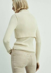 Ribbet cremesweater med høj krave og cropped design, parret med lyse beige tætsiddende jeans. Blød tekstur og slanke pasform detaljer.