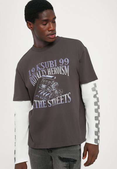 Grafisches T-Shirt in Dunkelgrau mit langen weißen Ärmeln, das ein Motordesign und den Text trägt: "19 KSUBI 99 ROYALTY HEROISM THE STREETS."