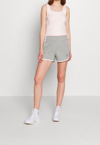 Camiseta sin mangas de color rosa claro con escote cuadrado, combinada con pantalones cortos grises con ribete blanco y un logo. Se lleva con zapatillas blancas de caña alta.