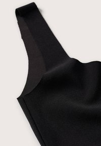 Gros plan d'un vêtement noir sans manches avec une large bretelle d'épaule et une texture de tissu lisse sur un fond clair.