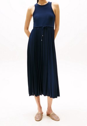 Robe côtelée bleu marine avec un corsage ajusté, une jupe plissée et une taille à cordon réglable. Associée à des chaussures slip-on tissées.