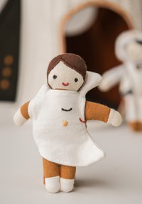 Zachte stoffen pop met bruin haar en een witte outfit, voorzien van oranje mouwen en kleine geborduurde gezichtskenmerken. Witte benen en een eenvoudig ontwerp.