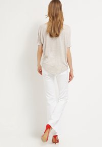 Light beige short-sleeve top paired with white flared pants and red high heels. Features smooth fabric and relaxed fit with rounded hem.